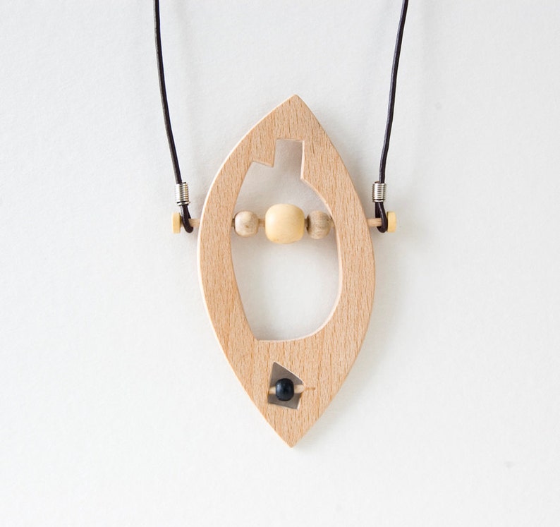 May include: A wooden pendant necklace with a unique shape and a black bead. The pendant is strung with wooden beads and hangs from a black cord.