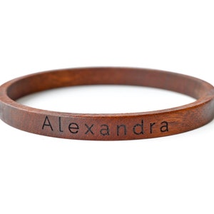 May include: A brown wooden bangle bracelet with the name "Alexandra" engraved on it.