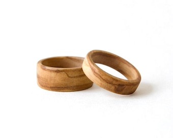 May include: Two rings crafted from light brown wood with visible natural grain patterns. One ring is wider with a flat outer surface, while the other is narrower with a slightly rounded profile. Both items feature a smooth, polished finish.