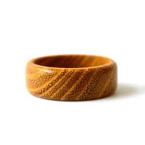Peut inclure: Une bague circulaire lisse fabriquée en bois brun clair. La surface de l'anneau présente un motif de grain naturel distinct avec des textures tourbillonnantes dans des tons de beige et de brun foncé, avec une finition polie et des bords arrondis.