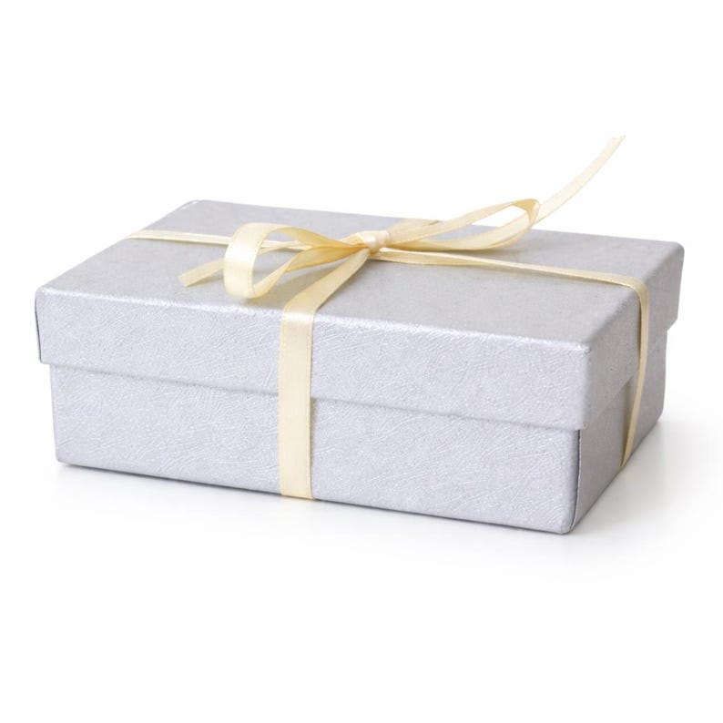 May include: A rectangular silver gift box with a textured surface, tied with a pale yellow satin ribbon. The ribbon is wrapped around the box and tied in a bow on top, suggesting a present or special occasion.