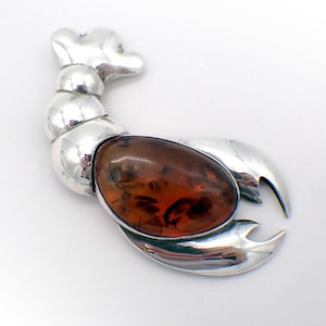 May include: A silver lobster brooch with a large, oval-shaped amber stone in the center. The lobster is detailed with a textured body and claws.