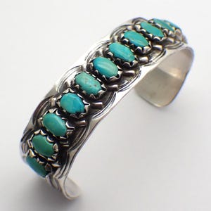 Puede incluir: Una pulsera de plata con incrustaciones de turquesa. La pulsera tiene un diseño decorativo y está hecha de plata de ley.