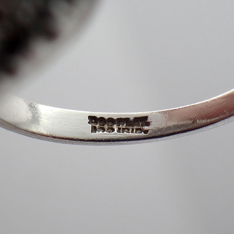 May include: Close-up of a silver ring with a hallmark that reads "925 ITALY". The ring's band is smooth and polished, reflecting the light. The ring is likely a piece of jewelry.