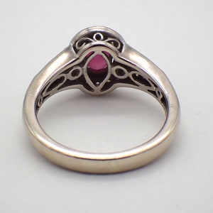 May include: A silver ring with a pink gemstone set in a filigree design.