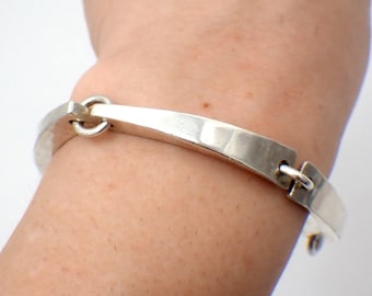 May include: A silver bangle bracelet with a hinged clasp. The bracelet is smooth and has a slightly curved shape.
