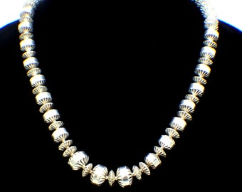 May include: A silver necklace with a series of round, textured beads. The beads are arranged in a symmetrical pattern.