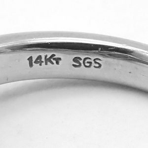 May include: Close-up of the inside of a gold ring with the inscription "14K" and "SGS" on the band.