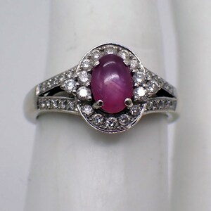 May include: A silver ring with a pink oval gemstone surrounded by a halo of smaller white gemstones.