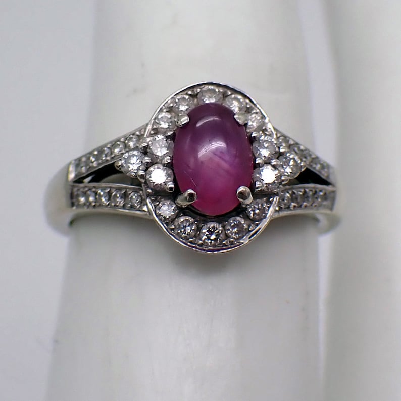 May include: A silver ring with a pink oval gemstone surrounded by a halo of smaller white gemstones.