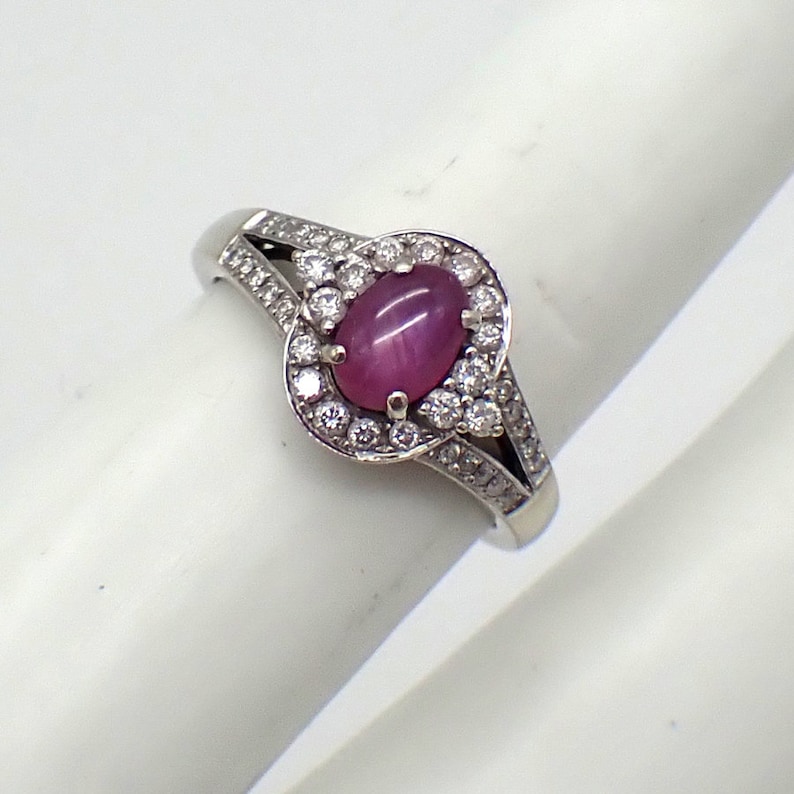 May include: A silver ring with a pink star ruby gemstone surrounded by a halo of smaller diamonds.