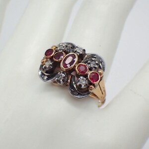 May include: A vintage ring with a gold band and a silver setting. The setting features a cluster of red rubies and white diamonds in a floral design.