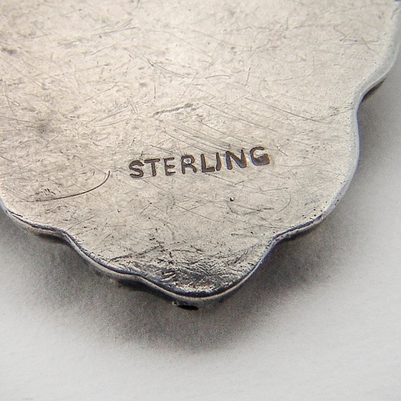 May include: Close-up of the back of a silver pendant with the word "STERLING" engraved on it.