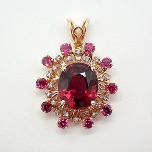 May include: A gold pendant featuring a large oval-shaped red gemstone surrounded by smaller red gemstones and diamonds in a floral design.