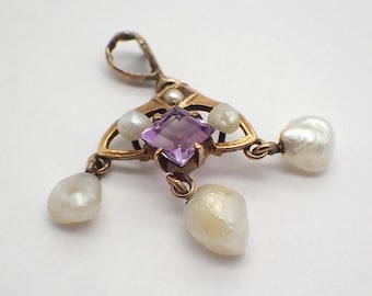 Puede incluir: Colgante dorado con una gema púrpura cuadrada central y cuatro perlas blancas. El colgante tiene un diseño ornamentado con un lazo en la parte superior para colgarlo. Las perlas tienen forma de lágrima y cuelgan del colgante.