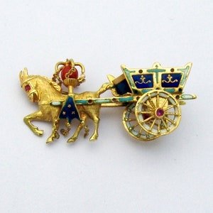 Op de afbeelding: Een broche van verguld metaal met een afbeelding van een paard dat een koets trekt. De koets is versierd met blauw en wit email en heeft één wiel. Het paard draagt een zadel van blauw en wit email en heeft een rode edelsteen op zijn hoofd.