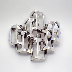 May include: A silver geometric brooch with a modern design. The brooch is made of interlocking squares and rectangles.