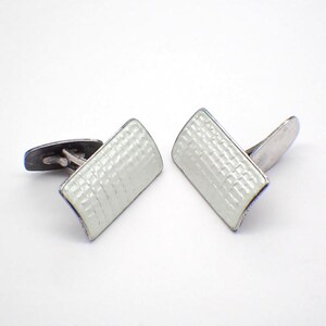 Peut inclure: Une paire de boutons de manchette en argent avec émail blanc. L'émail a un motif texturé.