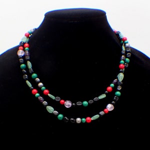 May include: A double strand necklace made of black, green, red, and purple beads. The necklace is made of various gemstones and is displayed on a black mannequin.