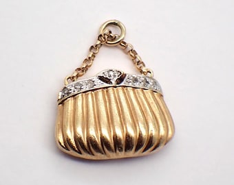 May include: A gold charm in the shape of a purse with a diamond-encrusted clasp. The purse has a chain attached to the top.