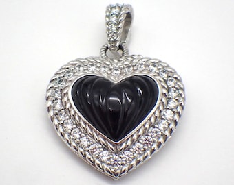Puede incluir: Un colgante de plata en forma de corazón con una piedra de ónix negro tallada rodeada de piedras de circonita cúbica transparentes.