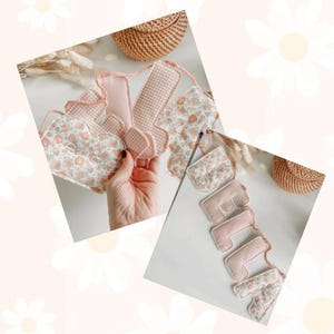 May include: A pink and floral fabric banner spelling out "little". The banner features a heart-shaped design and gingham and floral patterns. The banner is made of soft fabric and is likely for a baby or child's room.