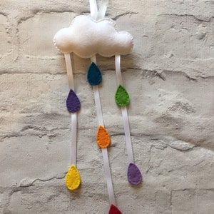 May include: A white felt cloud with rainbow colored felt raindrops hanging from it. The cloud is attached to a white ribbon.