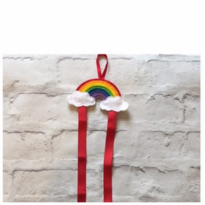 May include: A rainbow-colored felt rainbow with white felt clouds hanging from two red ribbon ties.