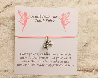 May include: A pink and white card with a silver fairy charm attached to a pink string bracelet. The card reads "A gift from the Tooth Fairy" and "Close your eyes to make your wish then tie this bracelet on your wrist when the bracelet breaks in two the wish you made may just come true."