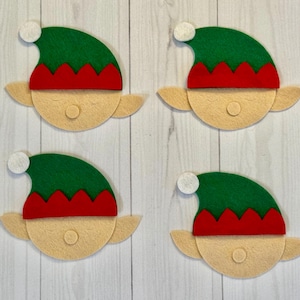 Puede incluir: Cuatro caras de duendes de fieltro con sombreros verdes, adornos rojos y pompones blancos. Las caras son de color beige con pequeñas narices redondas y orejas puntiagudas. Decoraciones festivas para Navidad.