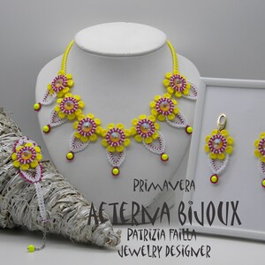 Könnte beinhalten: Eine gelbe und weiße Perlenkette mit rosa Akzenten, dazu passende Ohrringe und ein Armband. Die Halskette hat ein florales Design mit Kristall-Akzenten. Der Schmuck-Set ist mit "PRIMAVERA AETERNA BIJOUX PATRIZIA FAILLA JEWELRY DESIGNER" beschriftet.