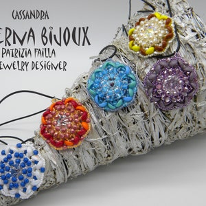 Pode incluir: Cinco pingentes de contas coloridas em um padrão de arco-íris, com um cordão preto. Os pingentes são redondos e têm um design de flor. O texto "CASSANDRA AETERNA BIJOUX PATRIZIA FAILLA JEWELRY DESIGNER" é visível na parte superior da imagem.