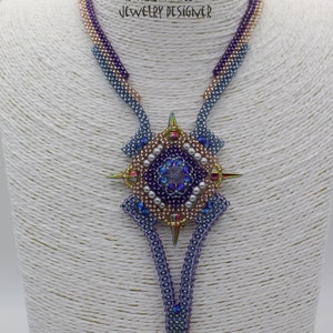 May include: A beaded necklace with a star-shaped pendant. The pendant is made of beads in shades of purple, blue, and gold. The necklace is on a white mannequin. The text "REVENGE AETERNA BIJOUX PATRIZIA FAILLA JEWELRY DESIGNER" is printed on the mannequin.