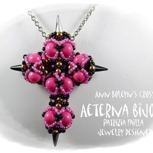May include: A pink and black beaded cross pendant necklace with silver chain. The pendant is a geometric design with spikes. The text "Ann Boleyn's Cross Aeterna Bijoux Patrizia Failla Jewelry Designer" is visible below the pendant.