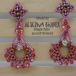 May include: A pair of chandelier earrings in shades of pink, red, and copper. The earrings feature a floral design with a central crystal and are adorned with small beads. The text "AETERNA BIJOUX" is visible.