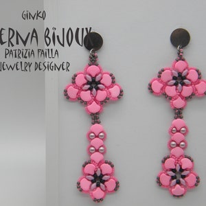 May include: A pair of pink and grey beaded earrings with a flower design. The earrings are labelled "Aeterna Bijoux" and "Patrizia Failla Jewellery Designer".