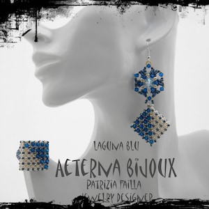May include: A pair of blue and white beaded snowflake earrings with a matching ring. The earrings are dangling and the ring is square shaped. The jewellery is displayed on a white mannequin head. The text "Laguna Blu Aeterna Bijoux Patrizia Failla Jewellery Designer" is displayed below the jewellery.