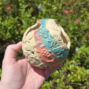 May include: A beige ceramic planter with a colorful design of sea turtles and other sea creatures. The planter has a rounded shape with a wide opening and is painted with blue and coral accents.