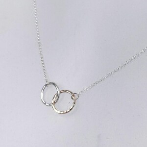 May include: A silver chain necklace with a delicate pendant featuring two interlocking circles, one silver and one gold.