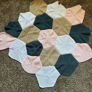 May include: A crocheted blanket made of hexagonal patches in shades of pink, white, brown, and green.