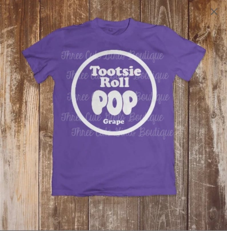 May include: A purple t-shirt with a white circle graphic that says 'Tootsie Roll POP Grape'.
