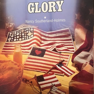 Op de afbeelding: Boekomslag van "The Americana Collection" met de titel "Old Glory". De afbeelding toont handgemaakte Amerikaanse vlaggen, een taart en een glas vloeistof. De vlaggen zijn rood, wit en blauw.