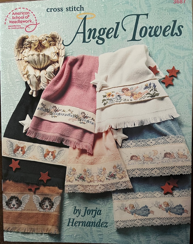 Puede incluir: Un libro de patrones de punto de cruz titulado "Angel Towels" de Jorja Hernandez. La portada presenta varias toallas con dise&ntilde;os de punto de cruz con tem&aacute;tica de &aacute;ngeles, incluyendo &aacute;ngeles, patrones florales y caras de perros. Las toallas son en tonos rosa, blanco, azul y beige.
