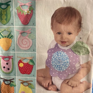 Könnte beinhalten: Simplicity-Schnittmuster 2273 mit verschiedenen Baby-Lätzchen-Designs. Die Lätzchen sind wie Früchte und Gemüse geformt, darunter eine Erdbeere, ein Apfel und eine Birne. Die Lätzchen sind in verschiedenen Farben gehalten und haben dekorative Elemente. Das Muster ist Einheitsgröße.