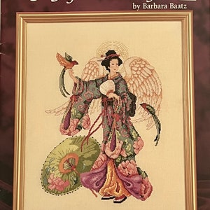 May include: Cross-stitch artwork titled "Japanese Angel" by Barbara Baatz, framed in gold. The image depicts a geisha-like figure with angel wings, holding a fan and a bird. The figure is adorned in a detailed floral kimono, with a parasol at her side.