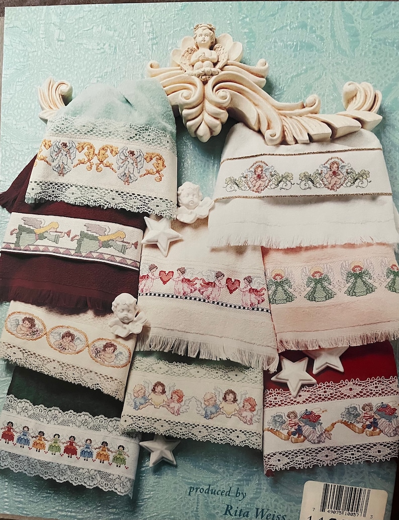 Puede incluir: Colecci&oacute;n de toallas bordadas con dise&ntilde;os de &aacute;ngeles. Las toallas presentan varios colores, incluyendo blanco, verde y burdeos, con patrones de punto de cruz detallados de &aacute;ngeles y adornos de encaje decorativos. La imagen tambi&eacute;n incluye figuritas de &aacute;ngeles decorativas y adornos en forma de estrella.