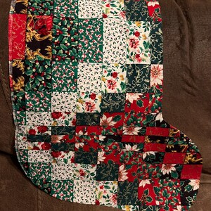 May include: A handmade Christmas stocking with a patchwork design. The stocking features squares of fabric in red, green, white, and black, with floral and holly patterns. The stocking is made of fabric and is designed for the holiday season.