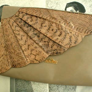 Könnte beinhalten: Eine beige Leder-Clutch mit einer großen, fächerförmigen Klappe aus braunem Schlangenleder. Die Klappe hat einen goldenen Metallverschluss mit dem eingeprägten Wort "Lauren".