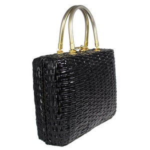 May include: A black woven handbag with a silver top handle and gold accents. The bag has a boxy shape and a woven texture.