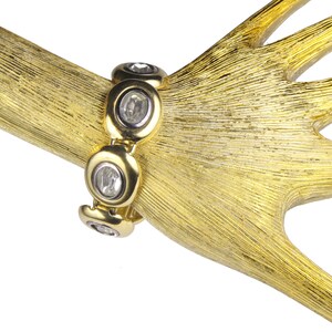 Puede incluir: Un brazalete dorado con piedras redondas transparentes engastadas en un dise&ntilde;o circular.